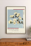 Portrait poster featuring white azalea blossoms against a pale blue background, with vertical Japanese and English text alongside minimalist red