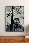 Portrait-style illustration featuring a telephone pole with crisscrossing wires, a traffic light, and a circular mirror reflecting the scene
