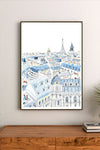 Framed artwork of a cityscape with blue and white buildings on a wall above a wooden cabinet.